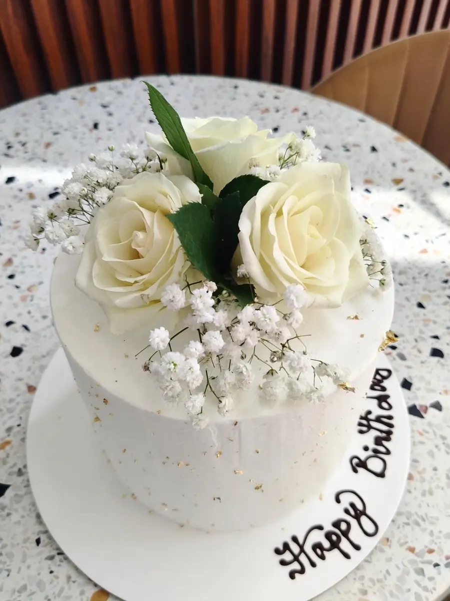 A white birthday cake with white roses and baby's breath, Happy Birthday piped on the board